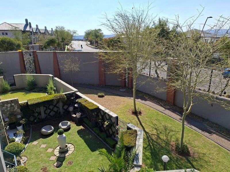An elevated view of a well-maintained private garden featuring a paved walkway, landscaped lawn, and secure boundary walling.