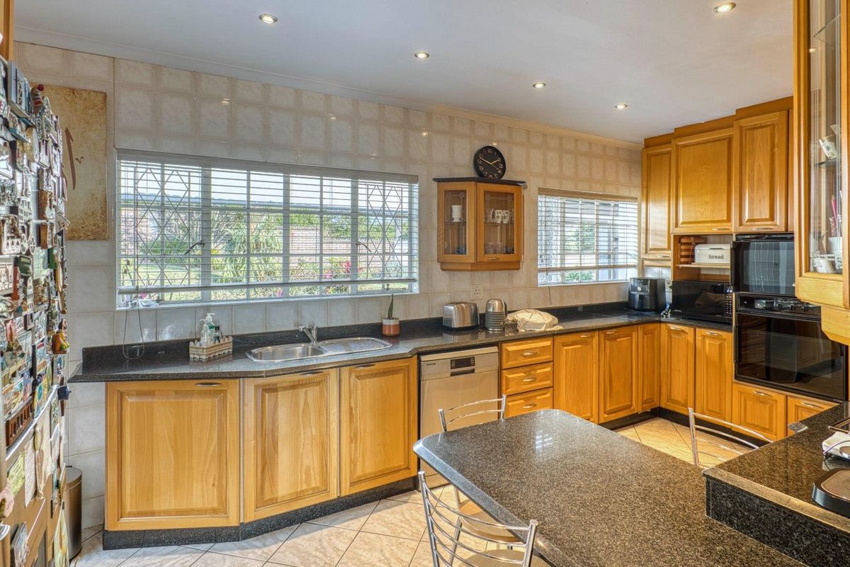 A functional kitchen featuring wooden cabinetry, granite countertops, a double sink, and built-in oven, with tiled backsplash and flooring throughout.