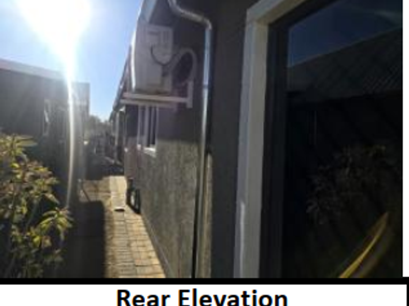 A view of the property's rear elevation featuring an external air conditioning unit and a paved side walkway.