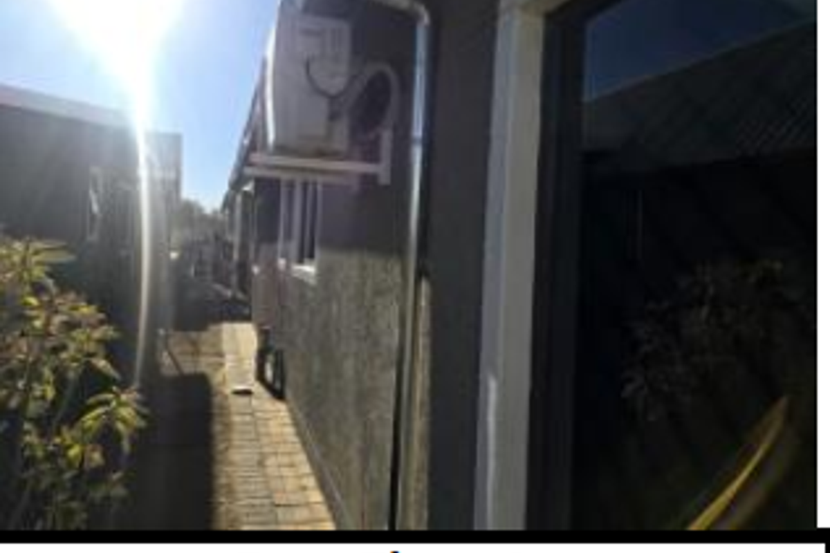 A view of the property's rear elevation featuring an external air conditioning unit and a paved side walkway.
