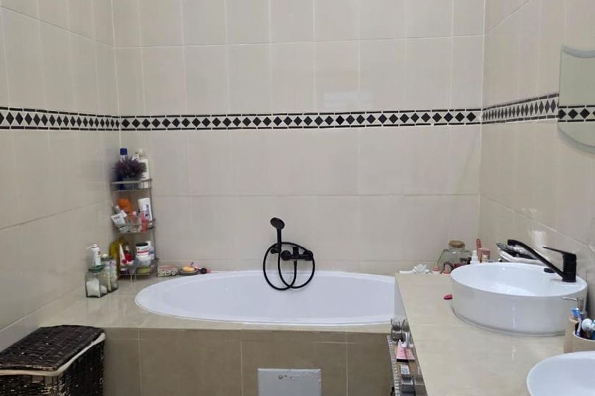 A functional bathroom featuring a built-in bathtub, dual vessel sinks on a tiled vanity, and full-height wall tiling with a decorative border.