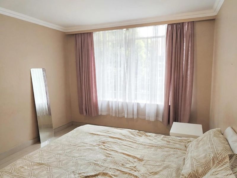A neutrally painted bedroom featuring tiled flooring, coving, and a large window dressed with layered curtains.