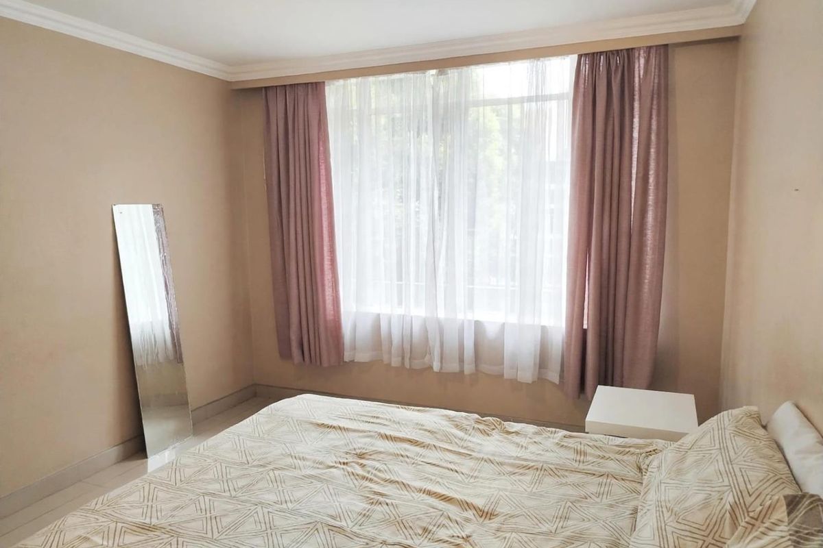 A neutrally painted bedroom featuring tiled flooring, coving, and a large window dressed with layered curtains.