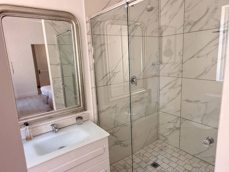 Modern bathroom featuring a vanity with integrated basin, glass-enclosed shower with marble-look wall tiles, and mosaic floor tiling.
