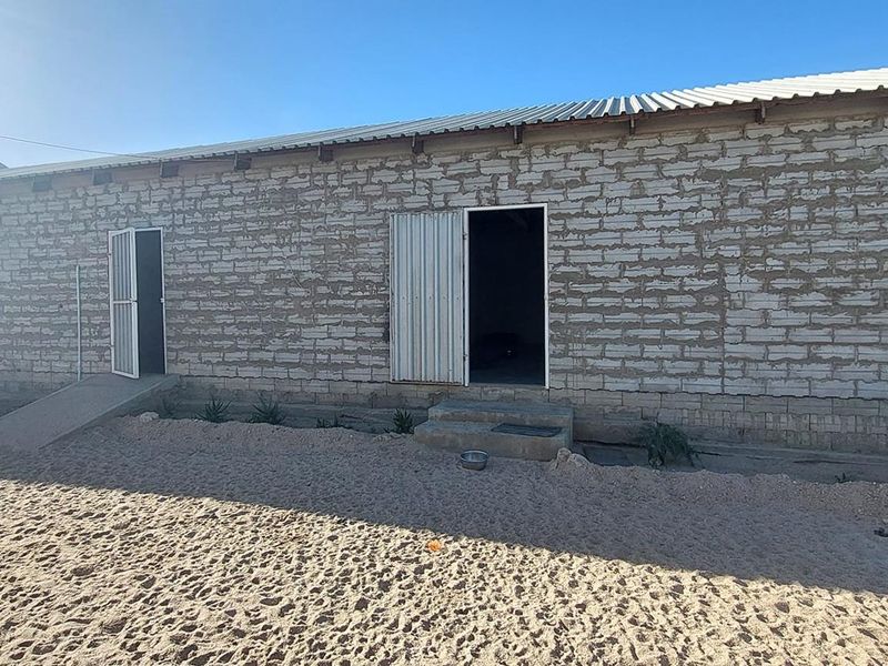Rear view of a stone masonry building featuring corrugated metal roofing, multiple metal security doors, and concrete access ramps.