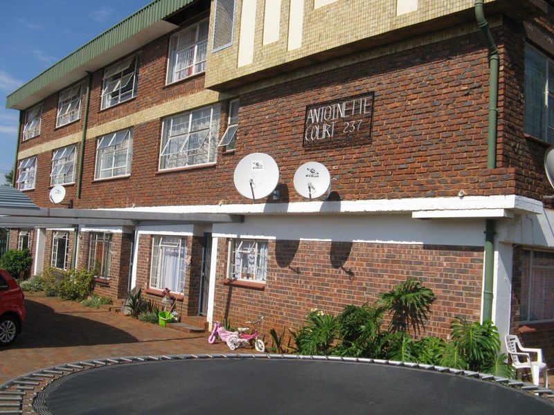 Exterior view of Antoinette Court apartment building featuring a brick facade, paved driveway, and multiple satellite dish installations.