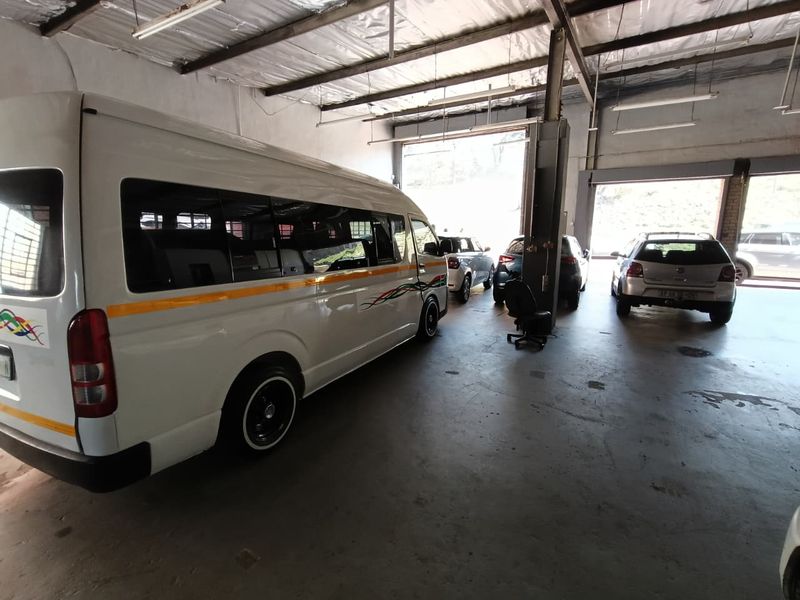 Spacious industrial garage featuring high ceilings with exposed steel trusses, concrete flooring, and large roller shutter doors for vehicle access.