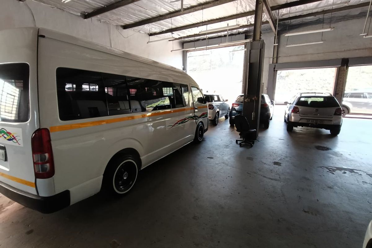 Spacious industrial garage featuring high ceilings with exposed steel trusses, concrete flooring, and large roller shutter doors for vehicle access.