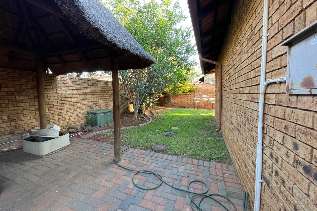 Rear garden area featuring a thatched lapa, brick paved patio, and established lawn with facebrick boundary walls.