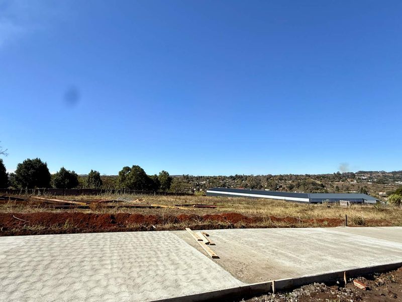 A view of a vacant commercial land plot featuring a newly laid concrete driveway and open, cleared terrain under a clear blue sky.