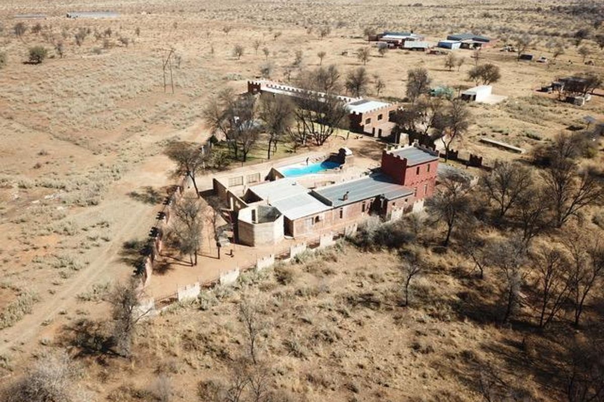 Aerial view of a small holding property featuring a main dwelling with turret architecture, a swimming pool, and surrounding arid landscape.