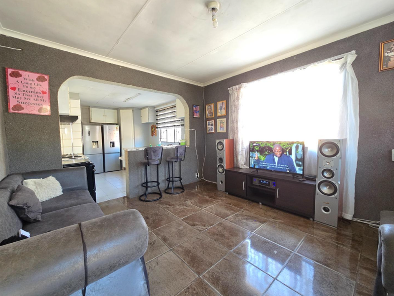 Open-plan living area featuring tiled floors, an arched transition to the kitchen, and a breakfast bar, offering a functional layout for daily living.