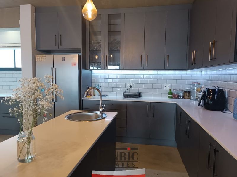 Modern kitchen featuring grey cabinetry, white quartz countertops, subway tile backsplash, and a functional island with an undermount sink.