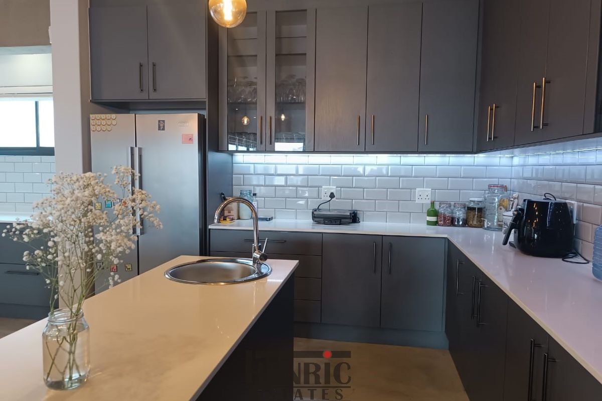 Modern kitchen featuring grey cabinetry, white quartz countertops, subway tile backsplash, and a functional island with an undermount sink.
