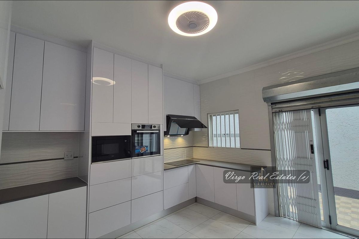 Modern kitchen featuring high-gloss white cabinetry, integrated appliances, tiled flooring, and direct access to an outdoor area through a sliding door with security gate.