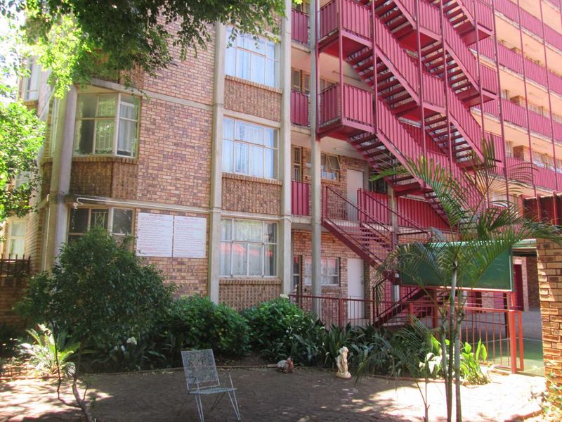 Rear view of an apartment building featuring a face brick facade and an external red steel staircase leading to upper levels.