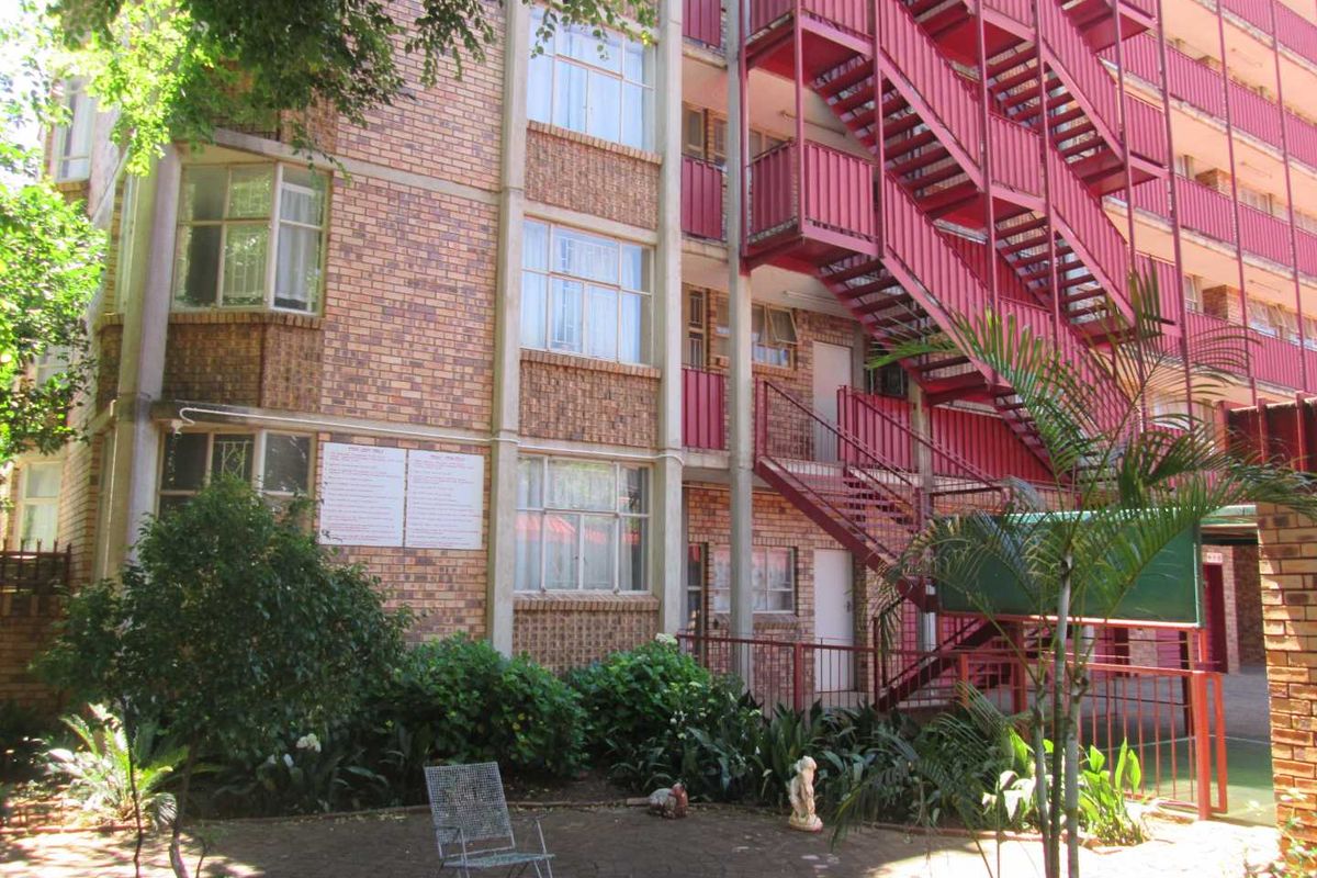 Rear view of an apartment building featuring a face brick facade and an external red steel staircase leading to upper levels.