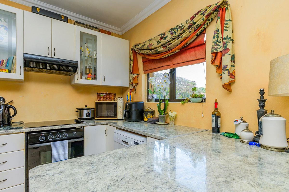 A functional kitchen featuring granite countertops, built-in oven, electric hob, extractor fan, and white cabinetry with glass-fronted display cupboards.
