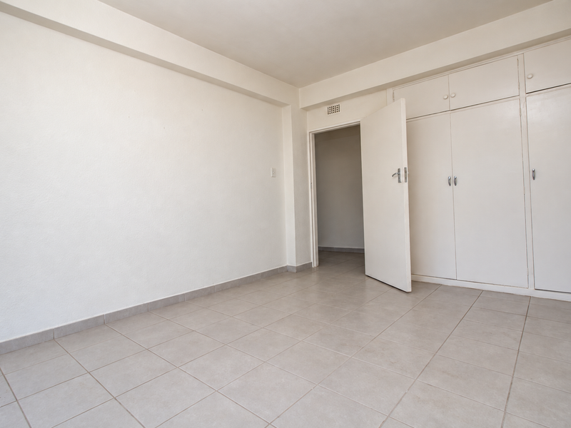 A bright, empty bedroom featuring neutral tiled flooring and ample built-in cupboard storage, offering a clean canvas for personalization.