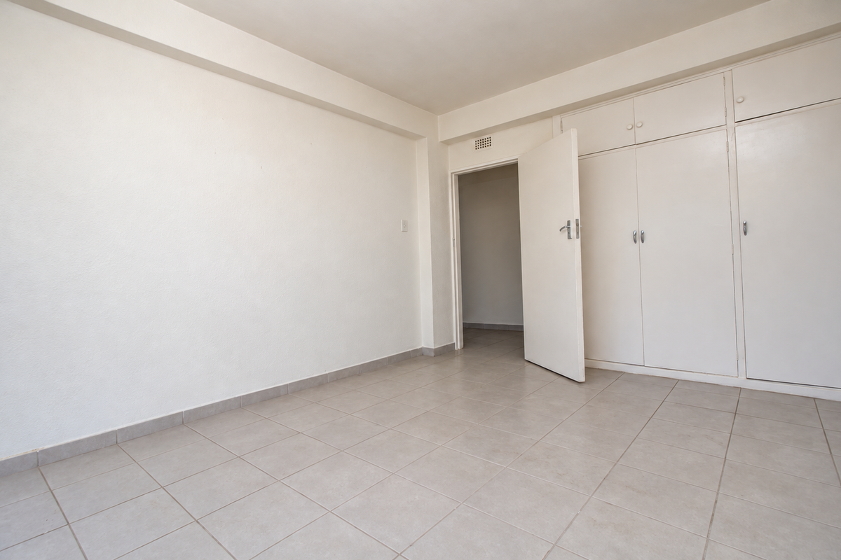 A bright, empty bedroom featuring neutral tiled flooring and ample built-in cupboard storage, offering a clean canvas for personalization.