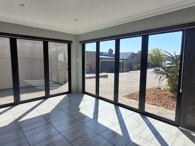 Bright and spacious living area featuring modern tiled flooring and large aluminium stacker doors that provide seamless access to the outdoor paved area.