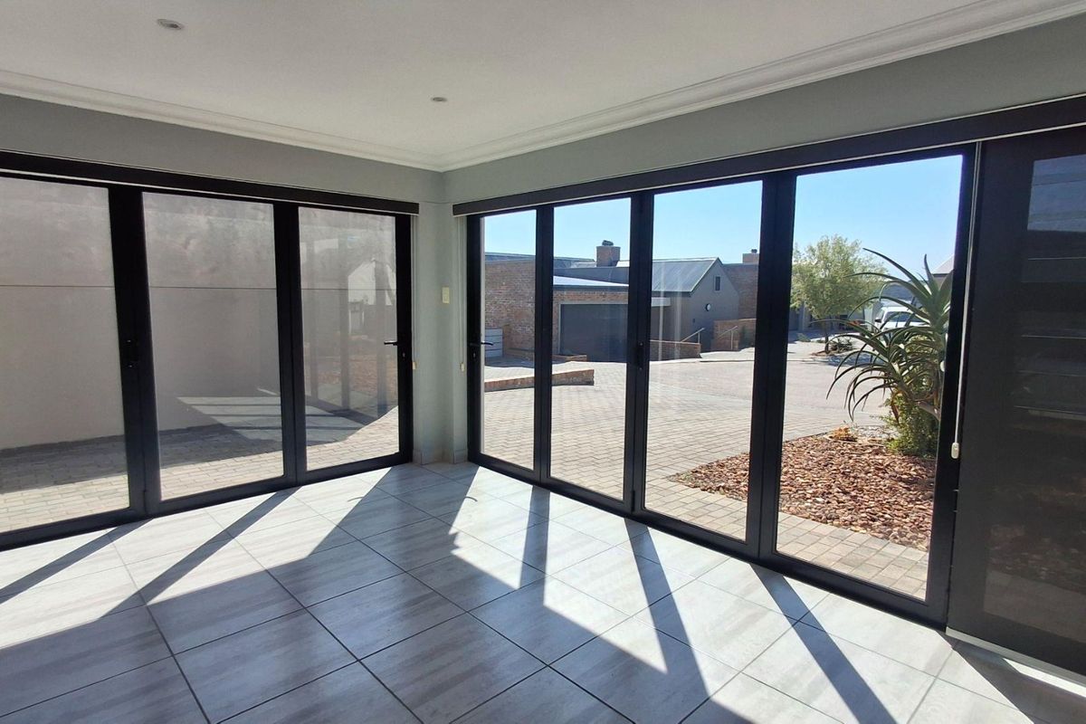 Bright and spacious living area featuring modern tiled flooring and large aluminium stacker doors that provide seamless access to the outdoor paved area.