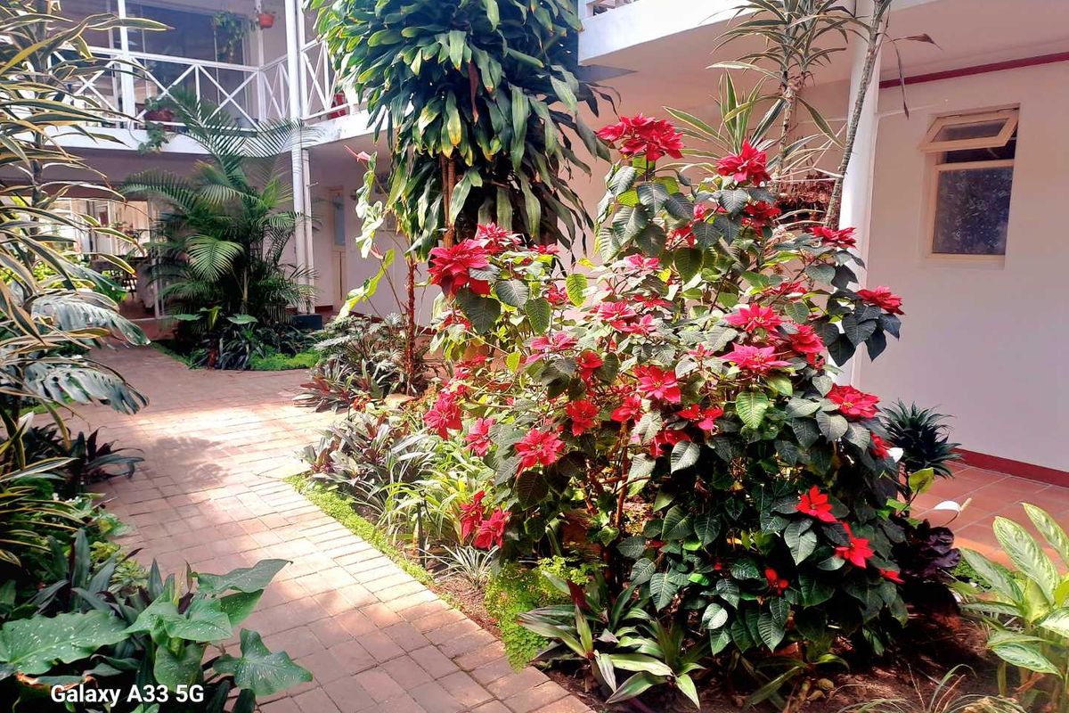 A well-maintained courtyard garden featuring brick paving and lush tropical landscaping, situated within an apartment complex with multi-level walkways.