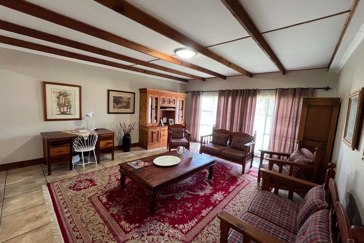 A spacious living room featuring exposed timber ceiling beams, tiled flooring, and large windows that provide ample natural light.