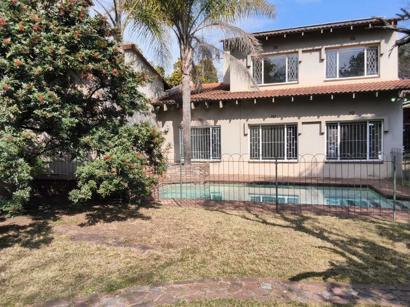 Rear view of a double-story cluster home featuring a swimming pool, security fencing, and a landscaped garden area.