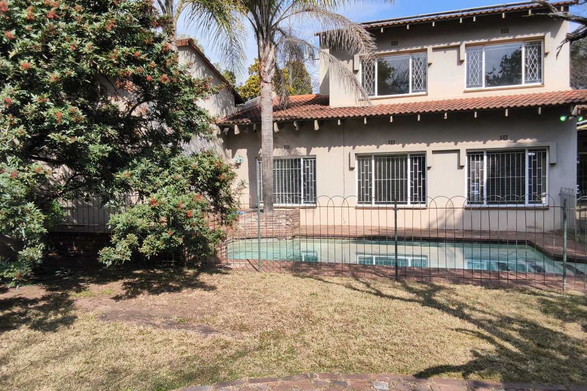 Rear view of a double-story cluster home featuring a swimming pool, security fencing, and a landscaped garden area.