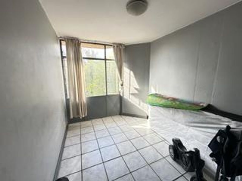 A vacant bedroom featuring tiled flooring and a large window, providing natural light. The space is ready for renovation or staging.
