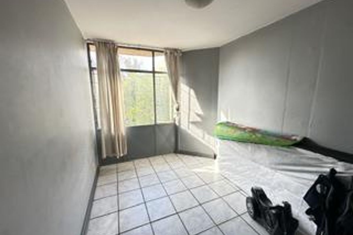 A vacant bedroom featuring tiled flooring and a large window, providing natural light. The space is ready for renovation or staging.