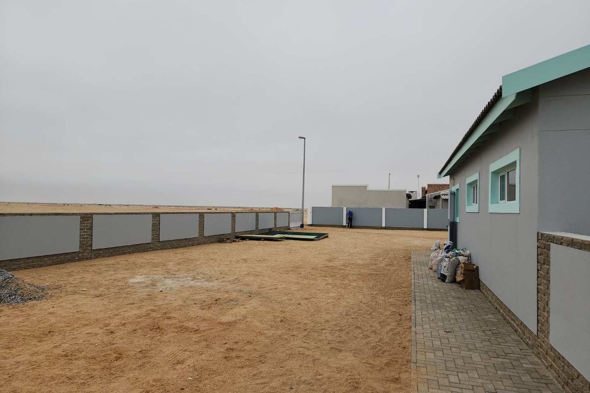 A spacious rear yard area featuring a paved walkway, perimeter boundary wall, and open sandy ground, providing a blank canvas for landscaping.
