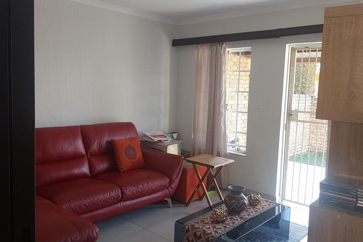 A living room featuring tiled flooring, a security gate leading to the exterior, and a ceiling-mounted spotlight.