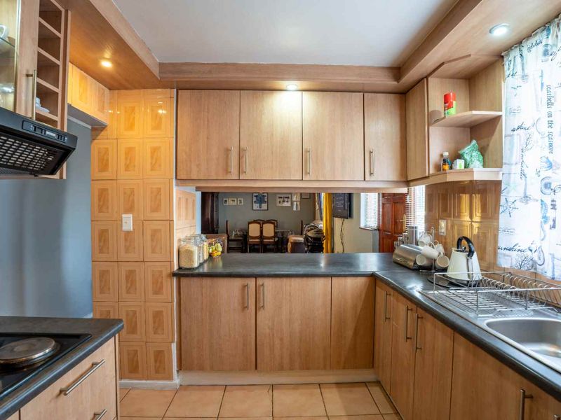 A functional kitchen featuring wood-finish cabinetry, laminate countertops, a built-in hob with extractor fan, and a pass-through window overlooking the dining area.