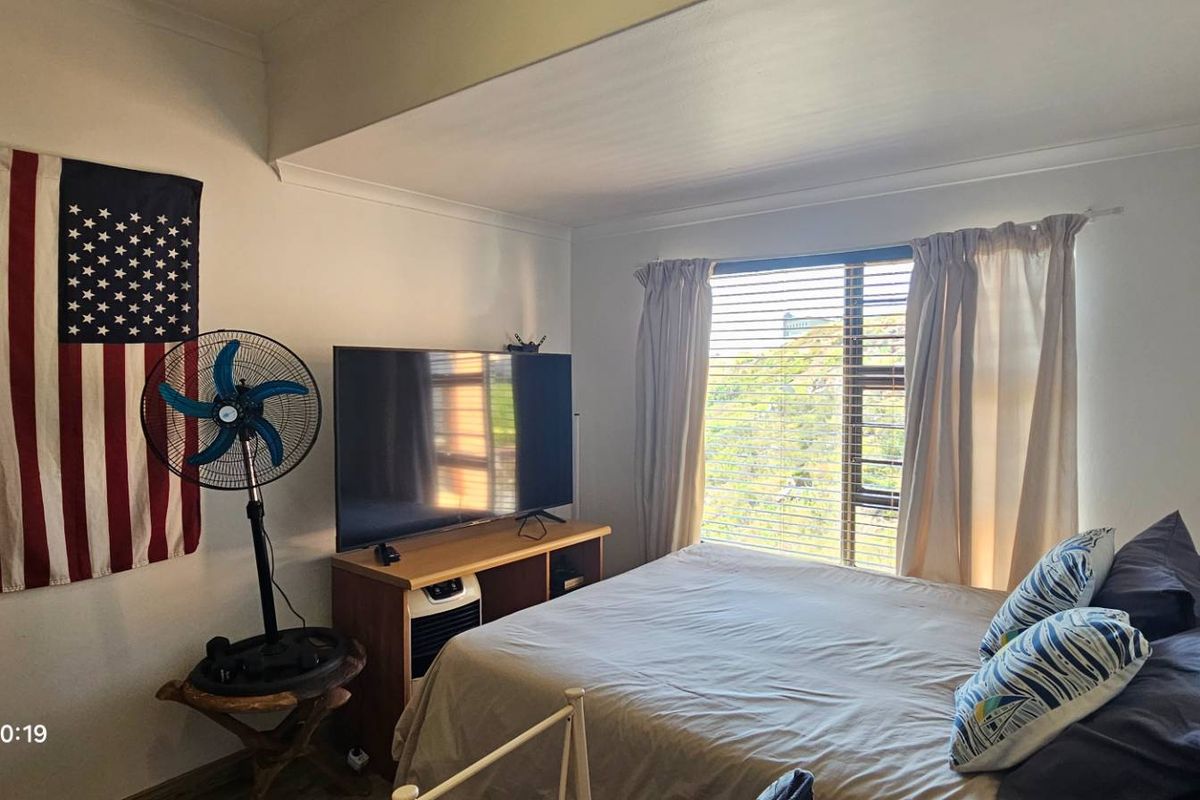 A functional bedroom featuring a large window with natural light, neutral wall finishes, and classic cove cornicing.