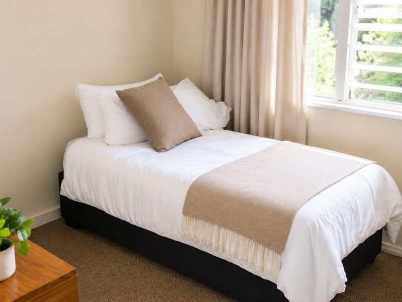 A cozy bedroom featuring neutral wall tones, carpeted flooring, and a functional louvre window allowing natural light.