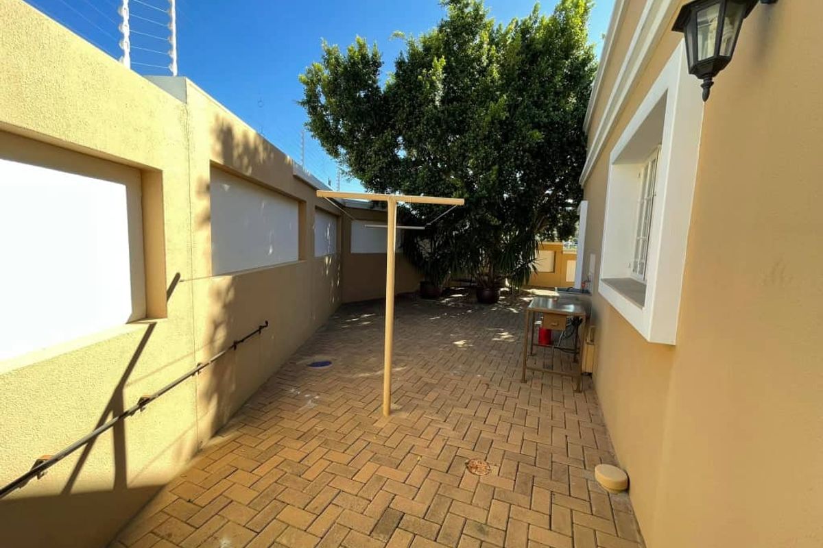 A paved rear courtyard area featuring perimeter walls with electric fencing and a wall-mounted light fixture.