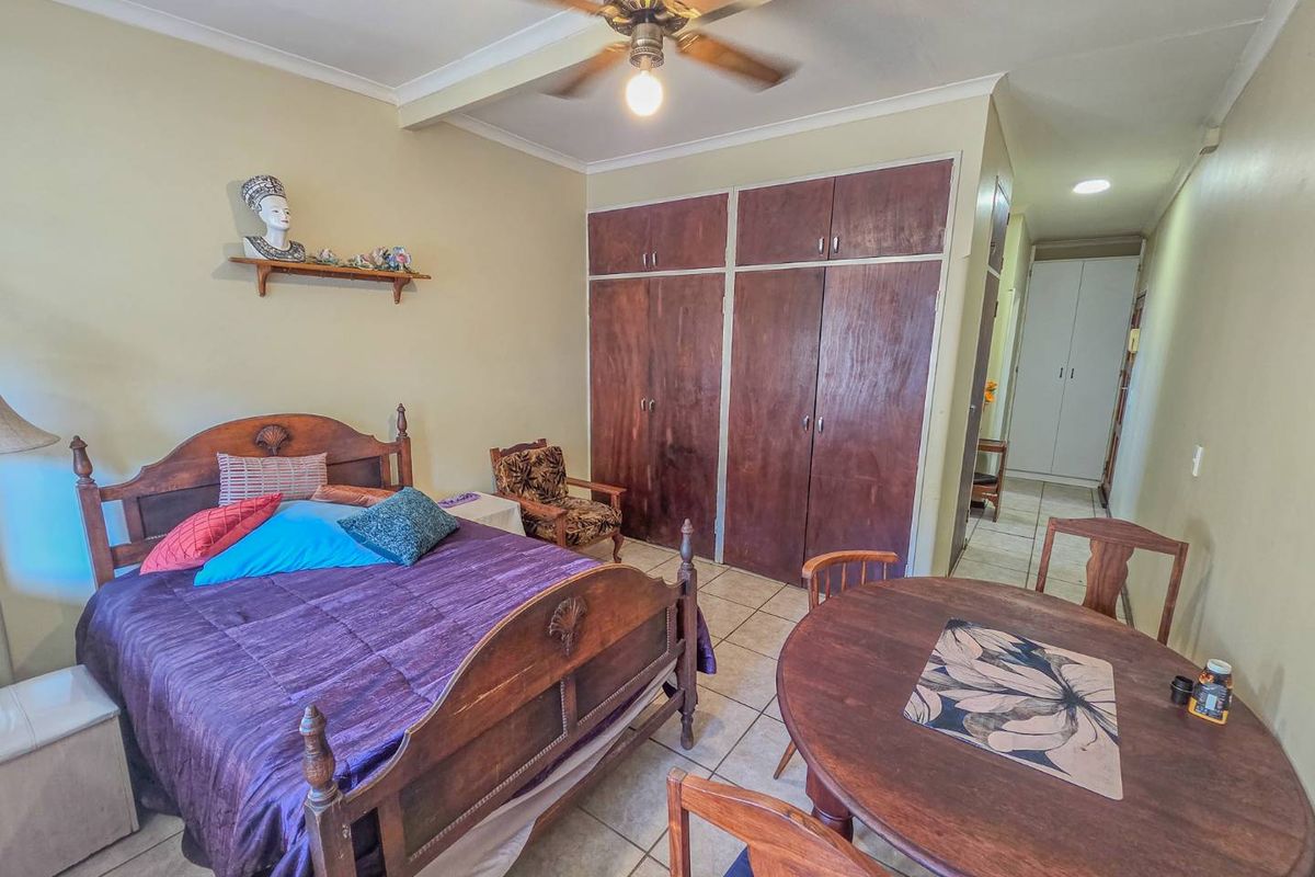 A bedroom featuring built-in wooden cupboards, a ceiling fan, and tiled flooring, offering a functional space with potential for modern updates.