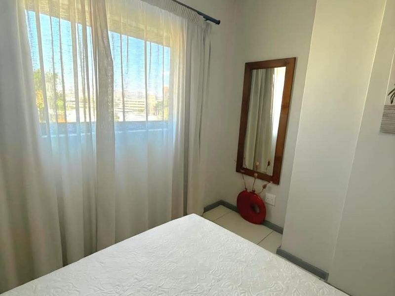 A bright bedroom featuring tiled flooring and a large window with curtains, offering a clean and neutral living space.