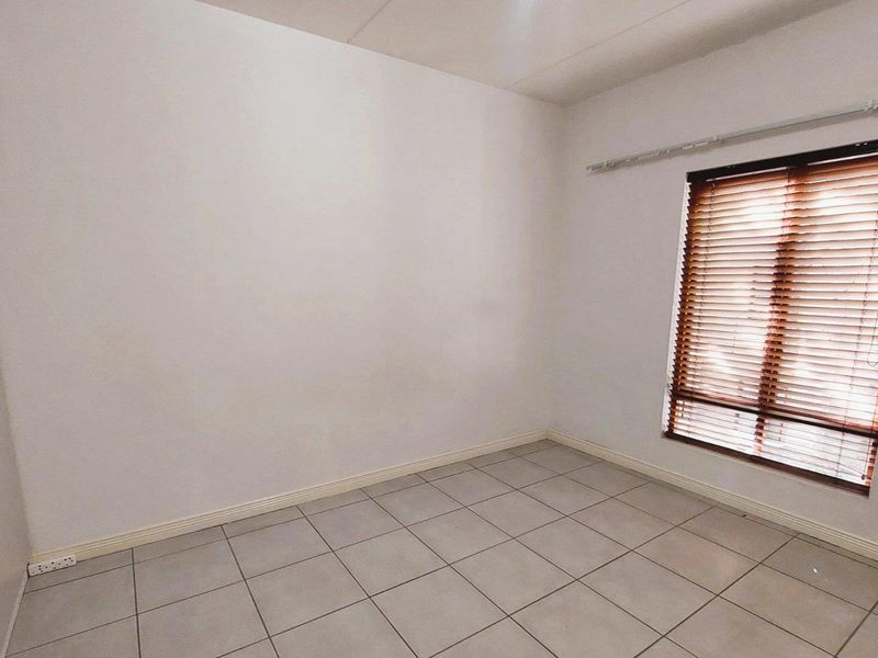A clean, empty bedroom featuring neutral tiled flooring, built-in cupboards, and venetian blinds, offering a versatile space ready for personalization.