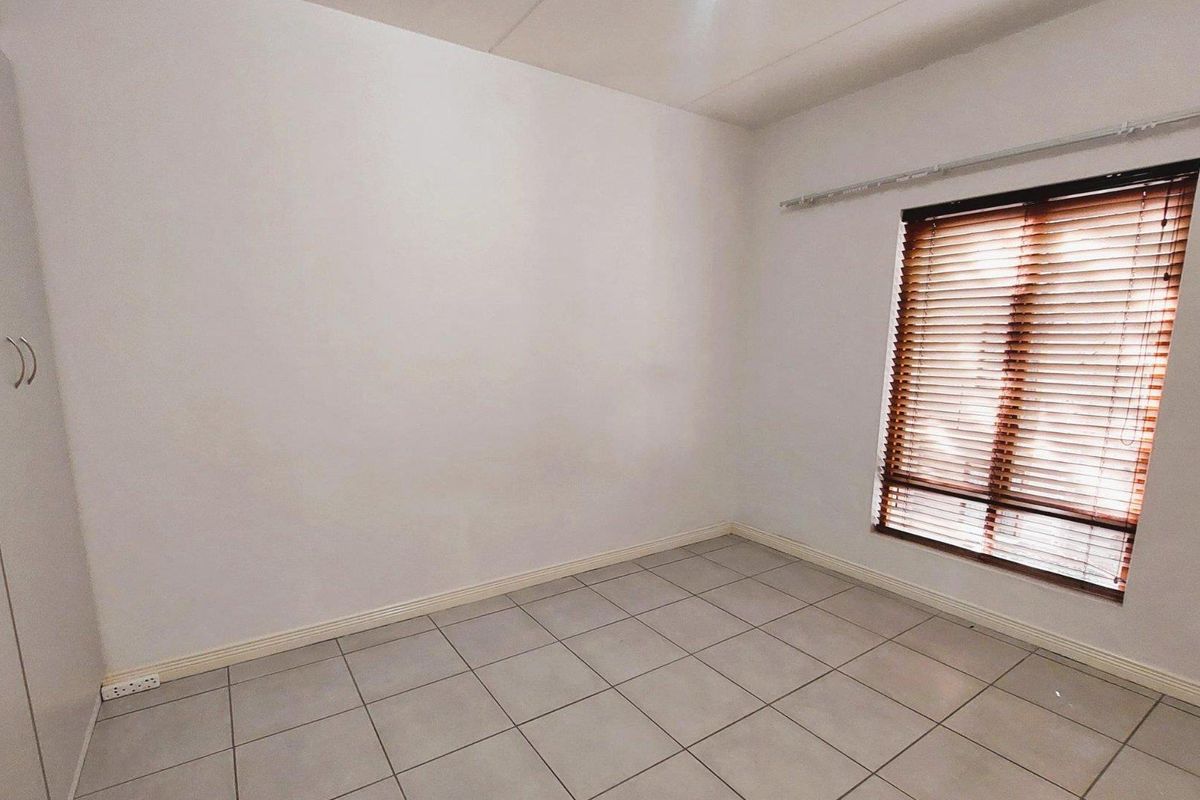 A clean, empty bedroom featuring neutral tiled flooring, built-in cupboards, and venetian blinds, offering a versatile space ready for personalization.