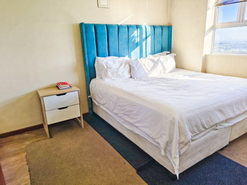 A bright bedroom featuring large windows with natural light and laminate flooring.