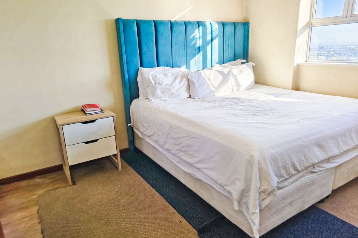 A bright bedroom featuring large windows with natural light and laminate flooring.