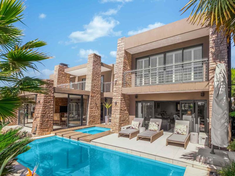 A modern rear exterior view featuring a swimming pool, stone-clad facade, and spacious patio area with access to the home's living spaces.