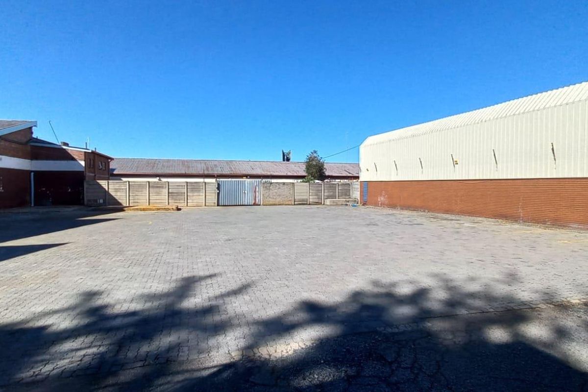 Spacious industrial yard area featuring paved surfacing, enclosed by perimeter walls and adjacent to large warehouse structures with metal cladding.