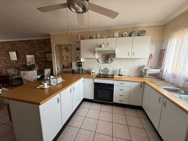 Functional kitchen featuring white cabinetry, laminate countertops, built-in oven, gas hob, and tiled flooring, with an open-plan layout connecting to the dining area.