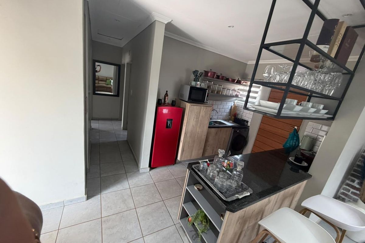 Modern kitchen featuring a central island with granite countertop, subway tile backsplash, and custom suspended shelving, flowing into a tiled hallway.