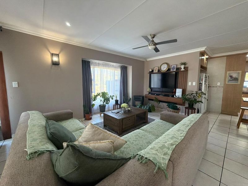 A comfortable living room featuring tiled flooring, a ceiling fan, and a built-in media unit, offering a functional and well-maintained living space.