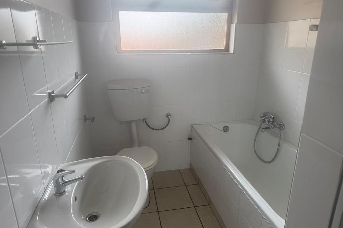 A functional, neutral-toned bathroom featuring a standard bathtub, pedestal basin, and toilet with white wall tiling and tiled flooring.